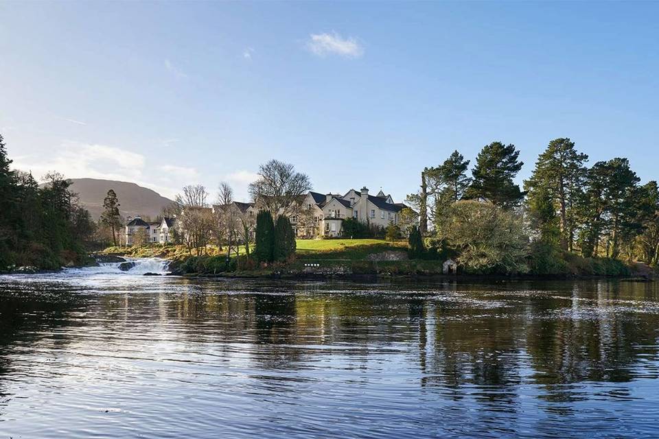 A hotel stands out amongst the trees from a view across the lakeside waters