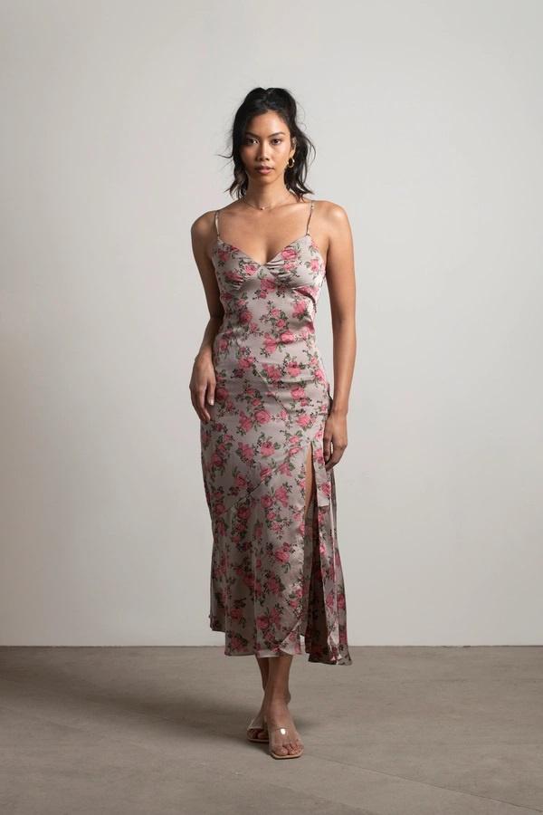 Model wearing light mocha-coloured slip-style dress. The dress has a slit on the right-hand side and pink floral designs throughout.