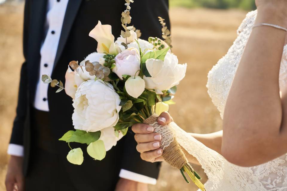 Newlyweds in a field, one holding a small bouquet wrapped in burlap