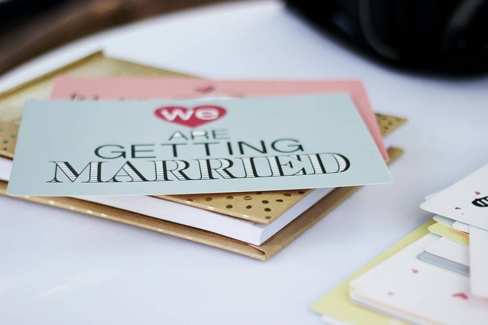 Wedding invitation on top of a notebook on a white desk. The invitation has 'We are getting married' in a bold font on the front.
