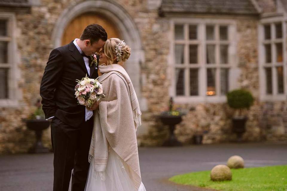 Newlywed couple standing outside a door on the exterior of the castle, their foreheads are pressed together