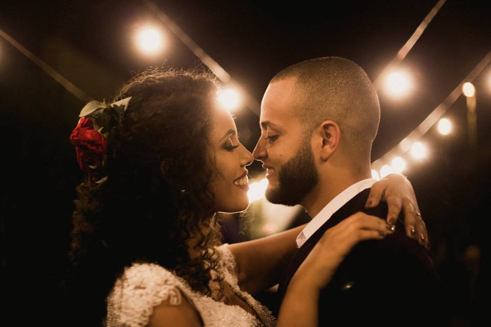 A couple smiling and dancing at night with fairy lights above them