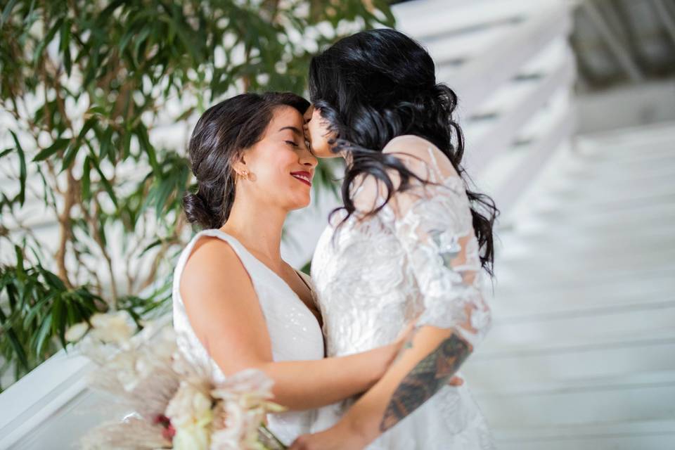 A bride kisses her bride on the forehead as they stand on the staircase