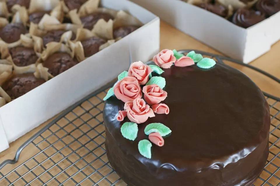 Chocolate cake with roses and leaves on one side near a box of muffins