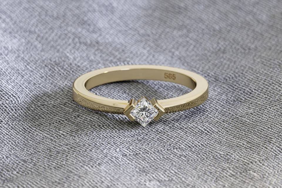 image of a simple gold princess cut engagement ring against a grey background